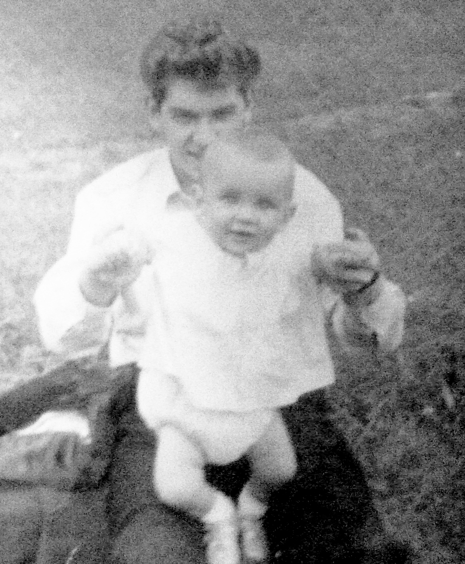 A young father steadying a baby taking first steps on rough grass, black and white